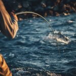 Angler fighting a large fish from a rocky shore, demonstrating the importance of correct fishing line strength.